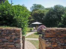 A stone wall entrance to a garden with a pathway leading to a seating area under an umbrella.