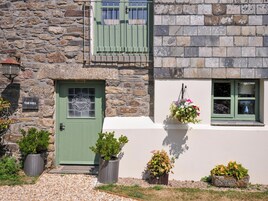 A stone building with a green door, a sign reading 'The Mill', and potted plants in front.