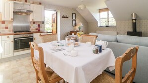Een gezellig eetgedeelte met een tafel voor twee, een keuken met moderne apparatuur, en een comfortabele zithoek met een bank en een open haard.