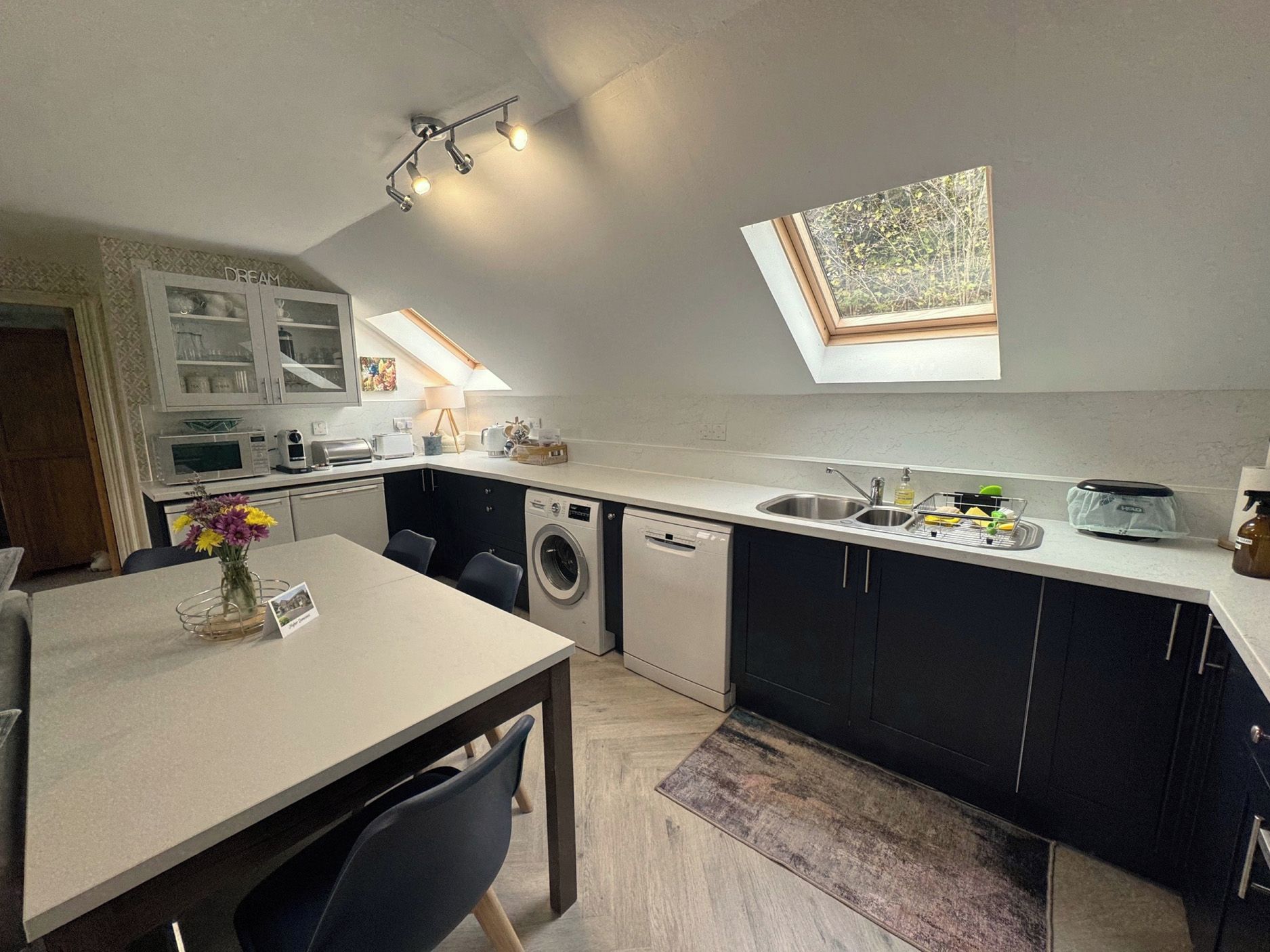 A compact kitchen with a dining area, a washing machine, a dishwasher, and a skylight.