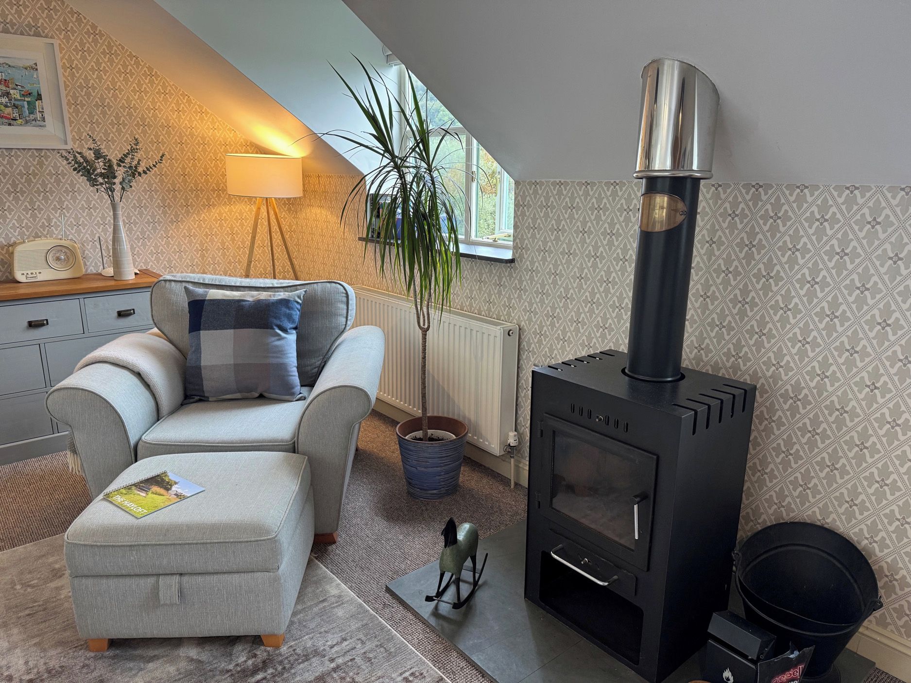 Ein gemütliches Wohnzimmer mit einer Couch, einem kleinen Tisch, einer Lampe, einem Blumentopf und einem Kaminofen.