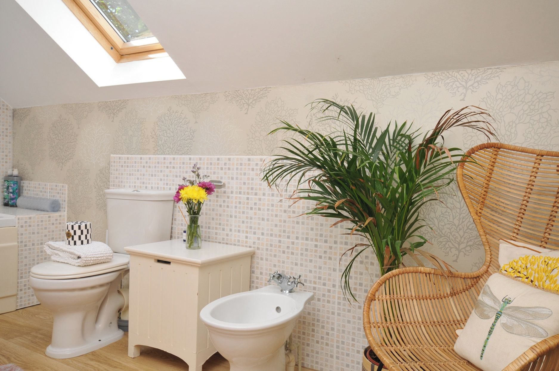 Ein Badezimmer mit Toilette, Bidet und Waschbecken, ein Korbstuhl und eine Pflanze.