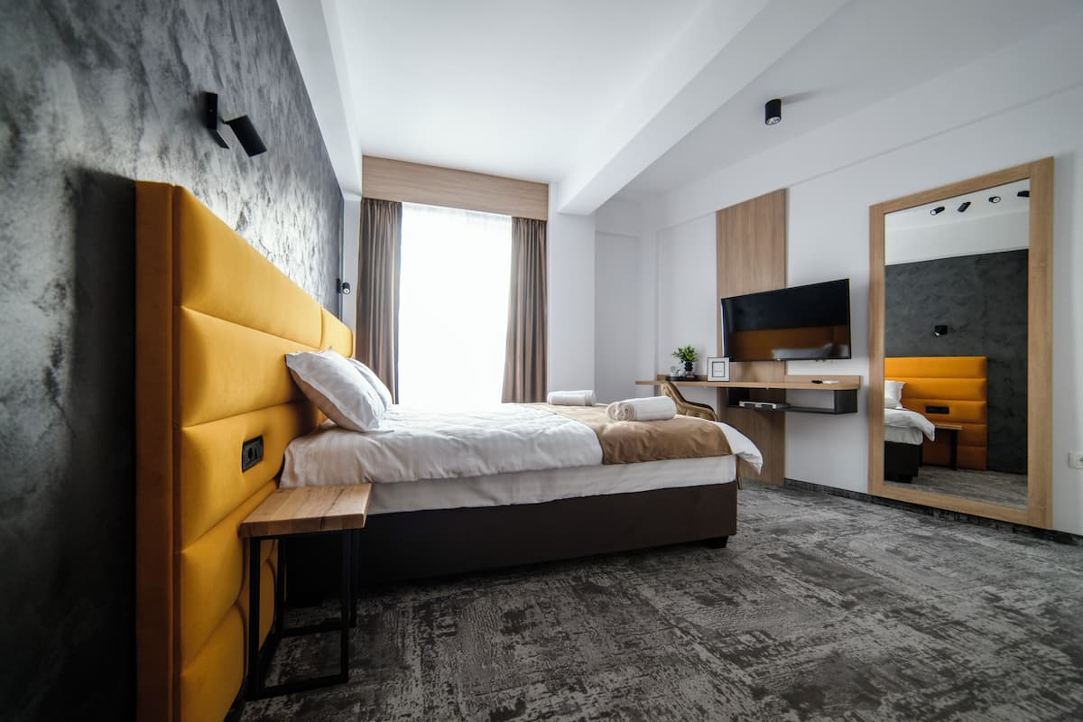 Una habitación de hotel moderna con una cama grande, un escritorio, un televisor de pantalla plana y un espejo amplio.