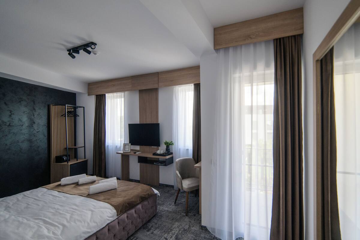 Una habitación de hotel moderna con una cama grande, un escritorio, una silla, un televisor y una ventana con cortinas.