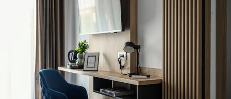 A modern room with a mounted TV, a blue chair, a wooden desk, and a plant.