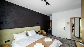 Ett hotellrum med en stor säng, ett nattduksbord, en stol, ett skrivbord och en spegel.