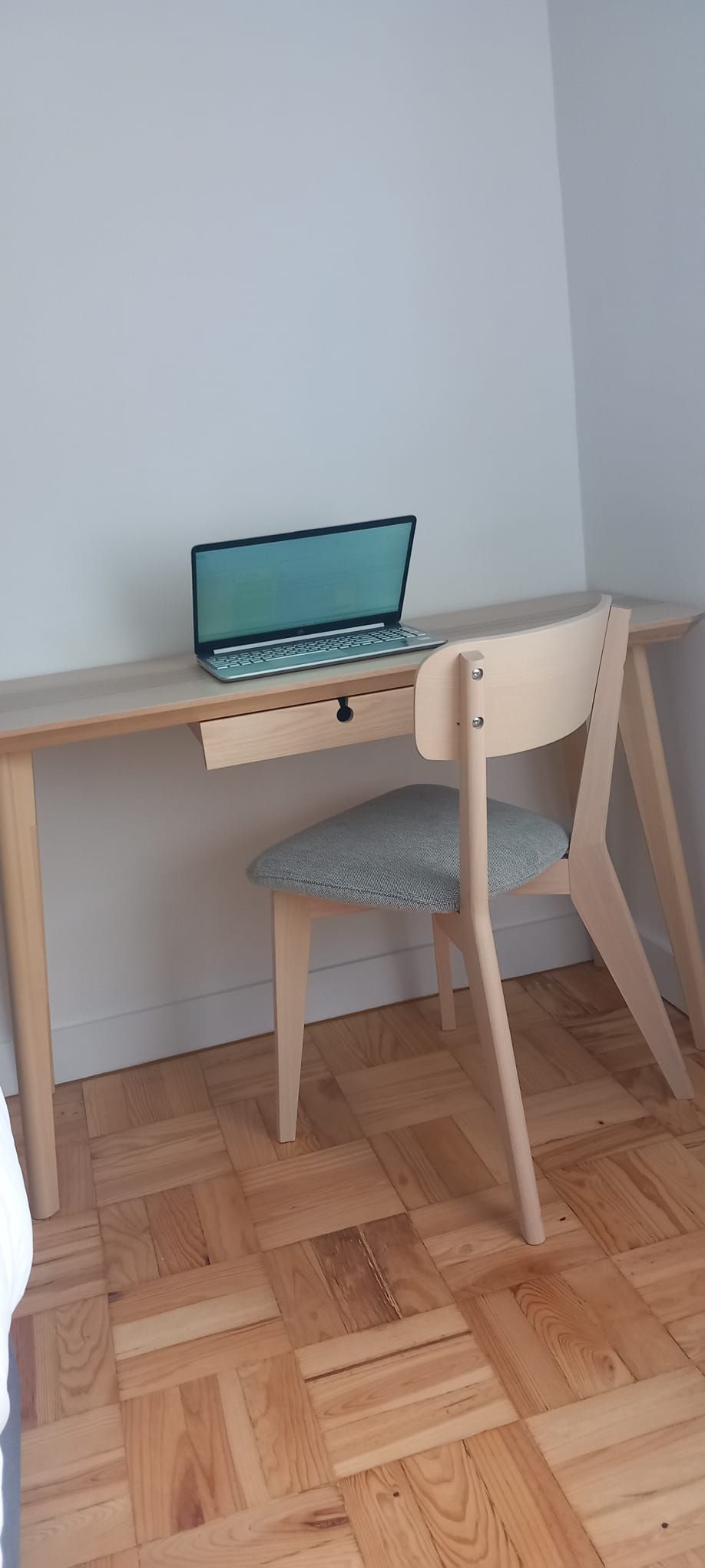 Een houten bureau met een laptop en een stoel met een zachte zitting.