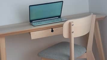 Een houten bureau met een laptop en een stoel met een zachte zitting.