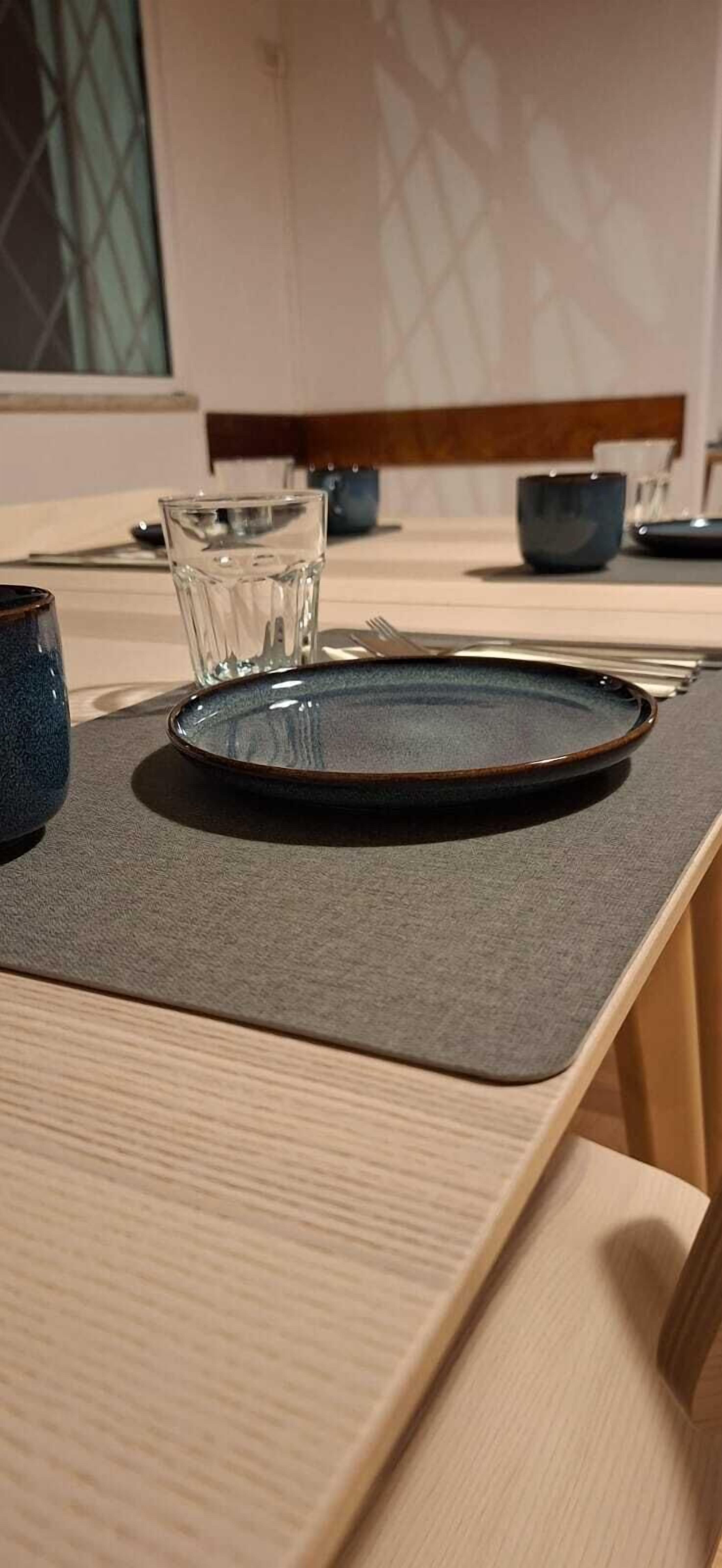 A dining table with a plate, a glass, and a dark-colored cup.