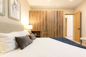 Un dormitorio con cama, almohadas, mesita de noche, lámpara y armario.