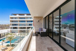 Un balcón moderno de hotel con piscina, mobiliario exterior y vistas a la ciudad.