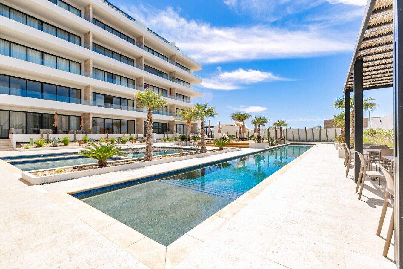 Un hotel moderno con piscina, zona de estar al aire libre y cielo azul despejado.
