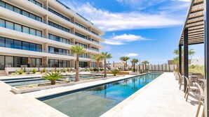 Un hotel moderno con piscina, zona de estar al aire libre y cielo azul despejado.