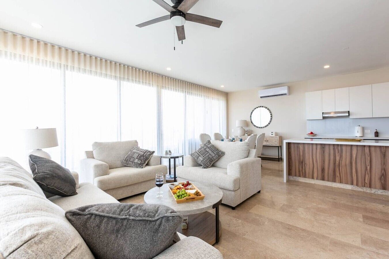 Una sala de estar moderna con un juego de sofá, una mesa de centro con fruta, y un comedor con mostrador de cocina.
