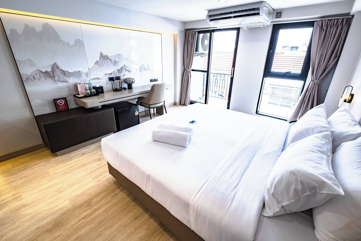 Een hotelkamer met een groot bed, een bureau met stoel, een wandairconditioner en uitzicht buiten door een raam.