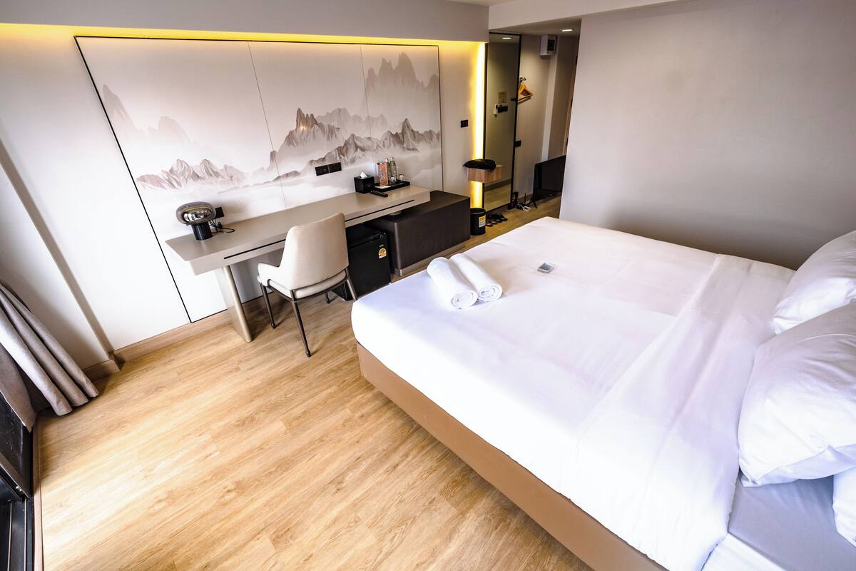 Een moderne hotelkamer met een groot bed, een bureau, een stoel en een aan de muur bevestigde televisie.
