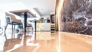 Un intérieur moderne avec un sol réfléchissant, un coin repas avec des chaises et des tables, et un espace cuisine avec des étagères et des appareils électroménagers.