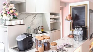 Une cuisine moderne équipée d’un four encastré, d’une machine à café et d’un petit réfrigérateur. On y trouve un plan de travail en marbre, un évier et une étagère contenant des ustensiles de cuisine.