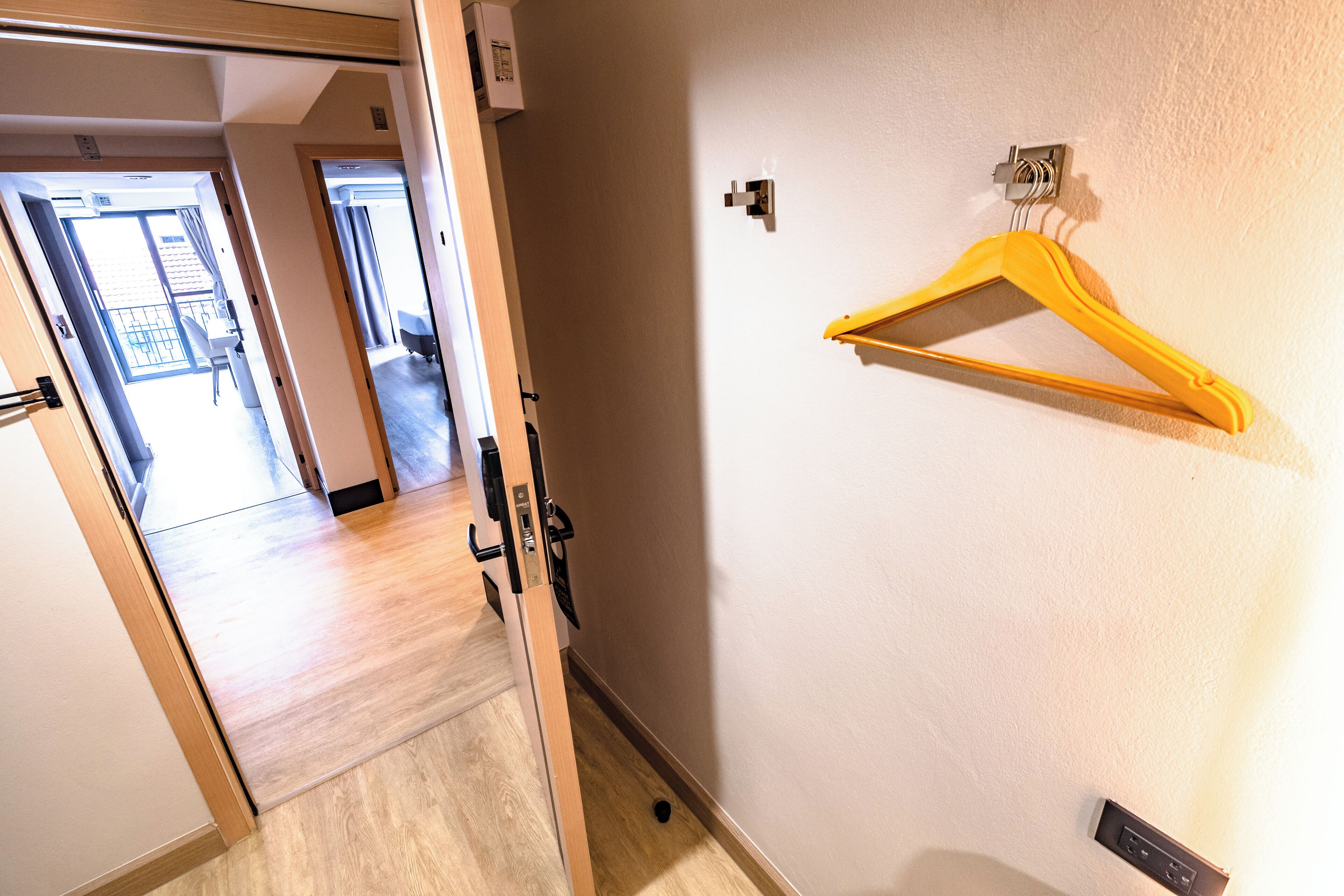 Un pasillo con piso de madera, un perchero amarillo en la pared y una puerta que da a otra habitación.