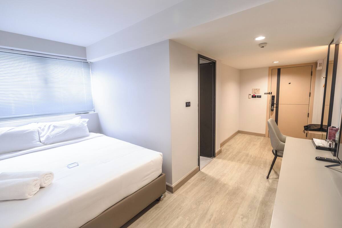 Een hotelkamer met een bed, een bureau en een stoel. Er is een deur die naar een andere kamer leidt.
