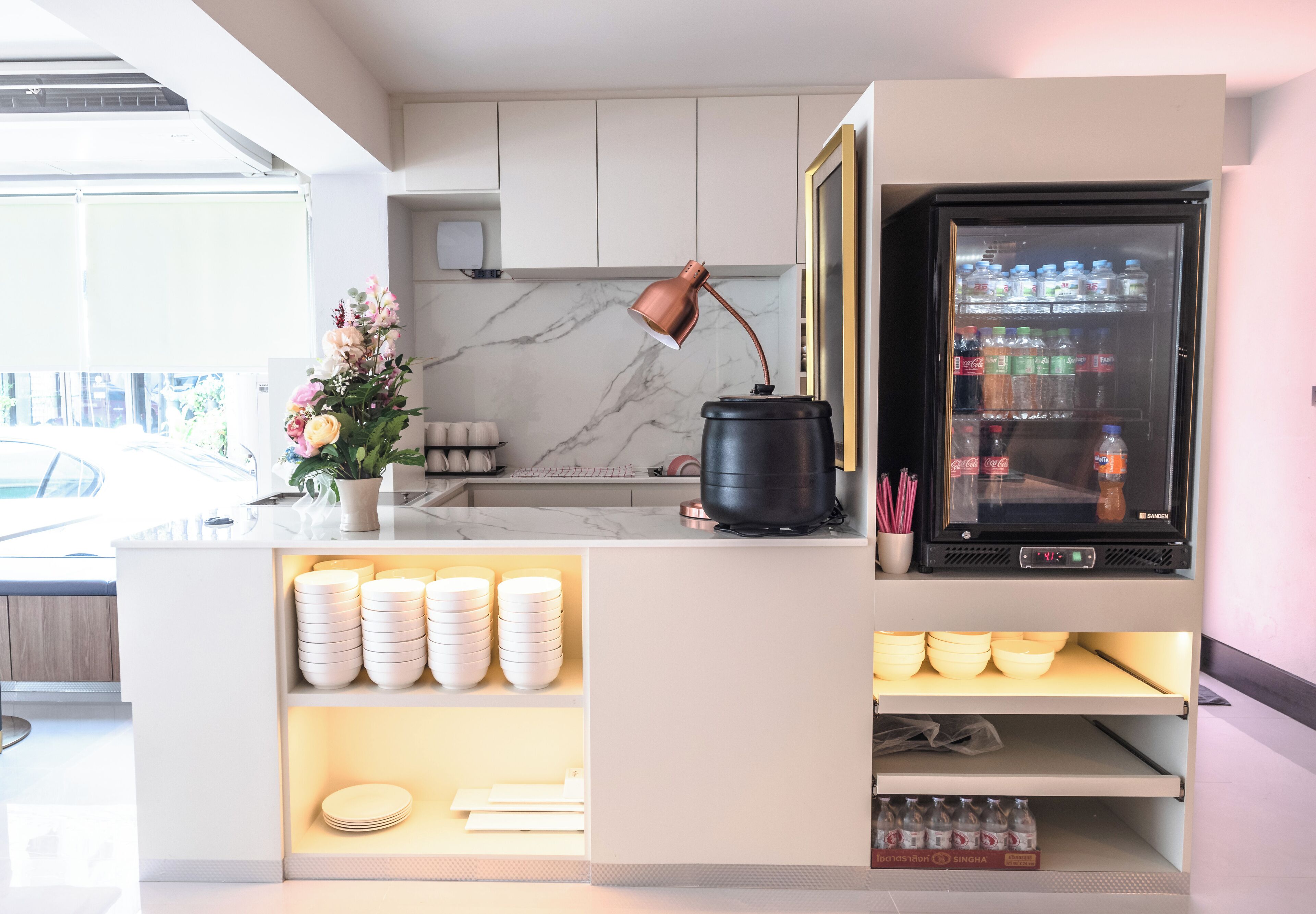 A modern kitchen with a marble backsplash, a coffee machine, a refrigerator stocked with beverages, and neatly arranged plates and bowls.
