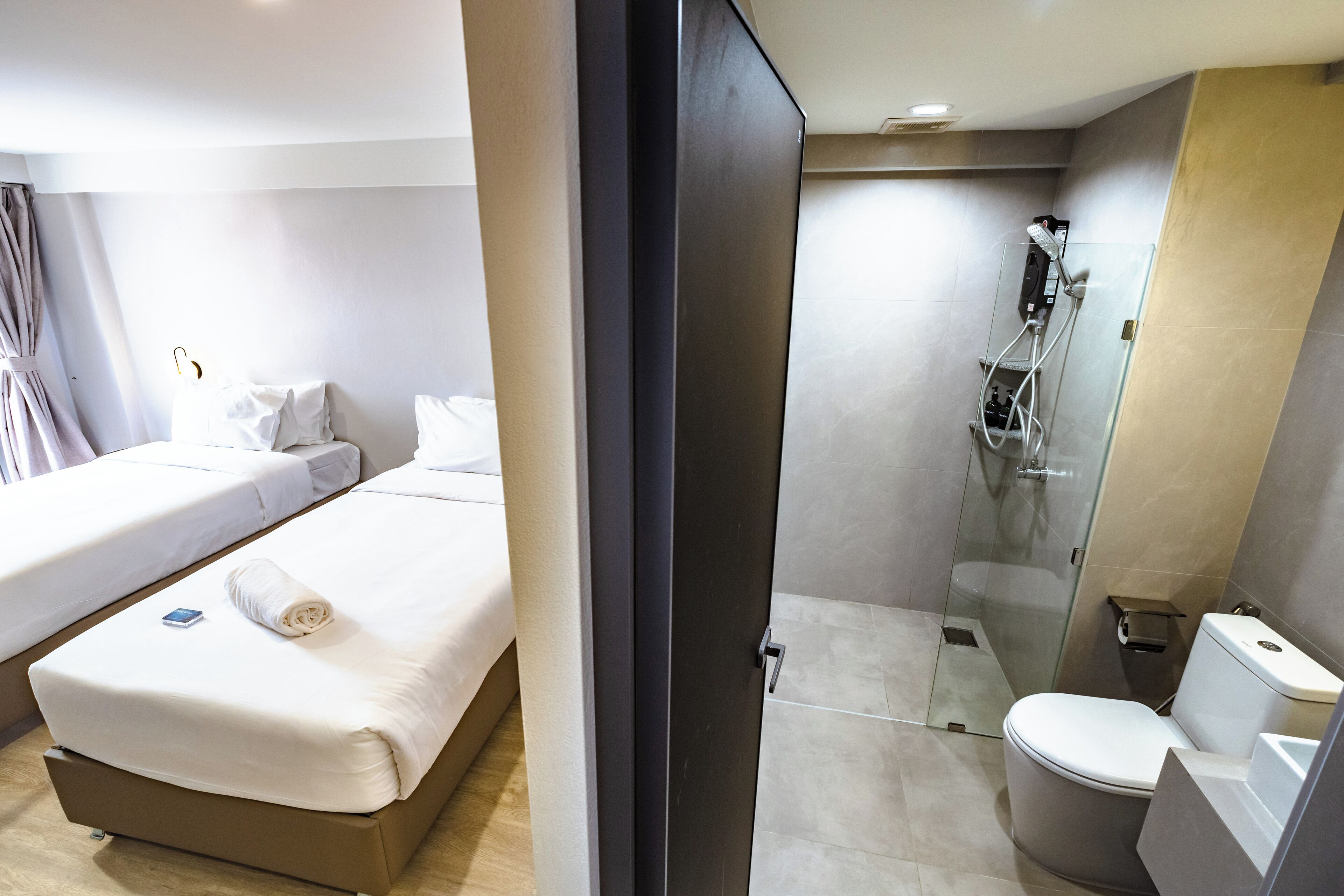 A hotel room with a bed, a bathroom with a toilet and shower, and a glass door separating the two areas.