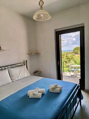 A bedroom with a bed, a blue bedspread, and two rolled towels on the bed.
