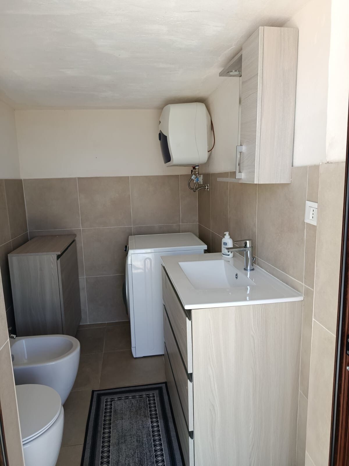 A compact kitchenette with a sink, a small washing machine, and a toilet.