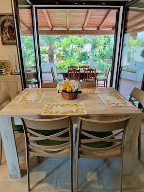 Comedor con una mesa dispuesta para cuatro personas, rodeada de sillas, y vista a un jardín a través de puertas de vidrio grandes.