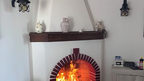 A living room with a brick fireplace, a grey sofa with a patterned cushion, and a wooden cabinet with various items on top. - Your Stay at Villa Calipso - The Perfect Family Escape by the Sea (Taranto)