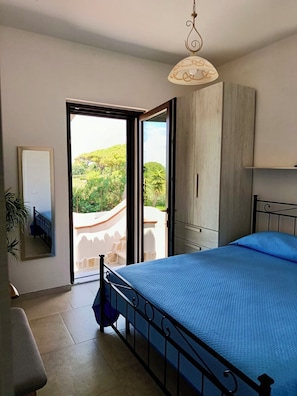 Una camera da letto con un letto, un armadio, uno specchio e vista su un giardino tramite una porta aperta.
