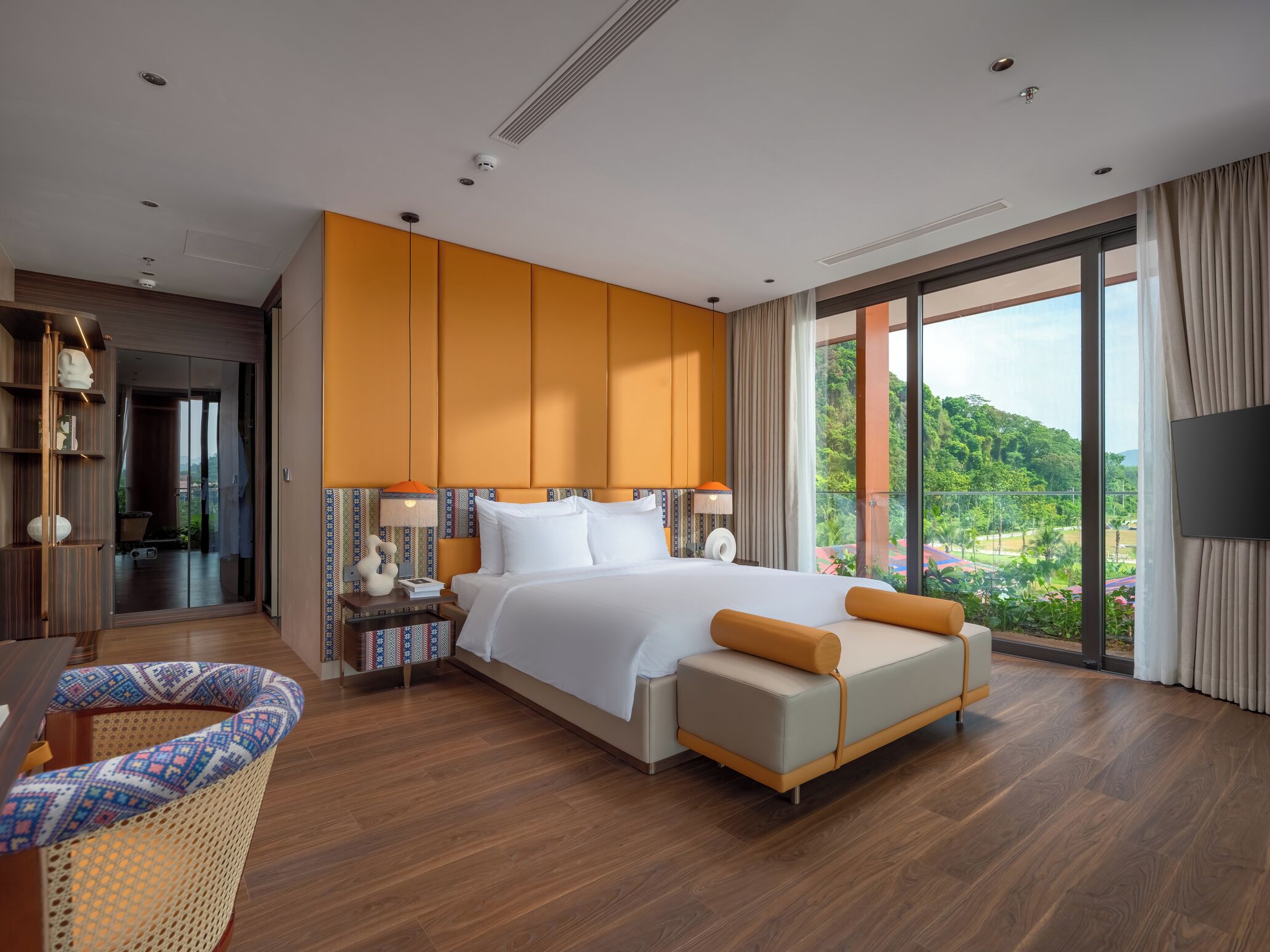 A modern hotel room with a large bed, a TV, and a balcony with a view of greenery.