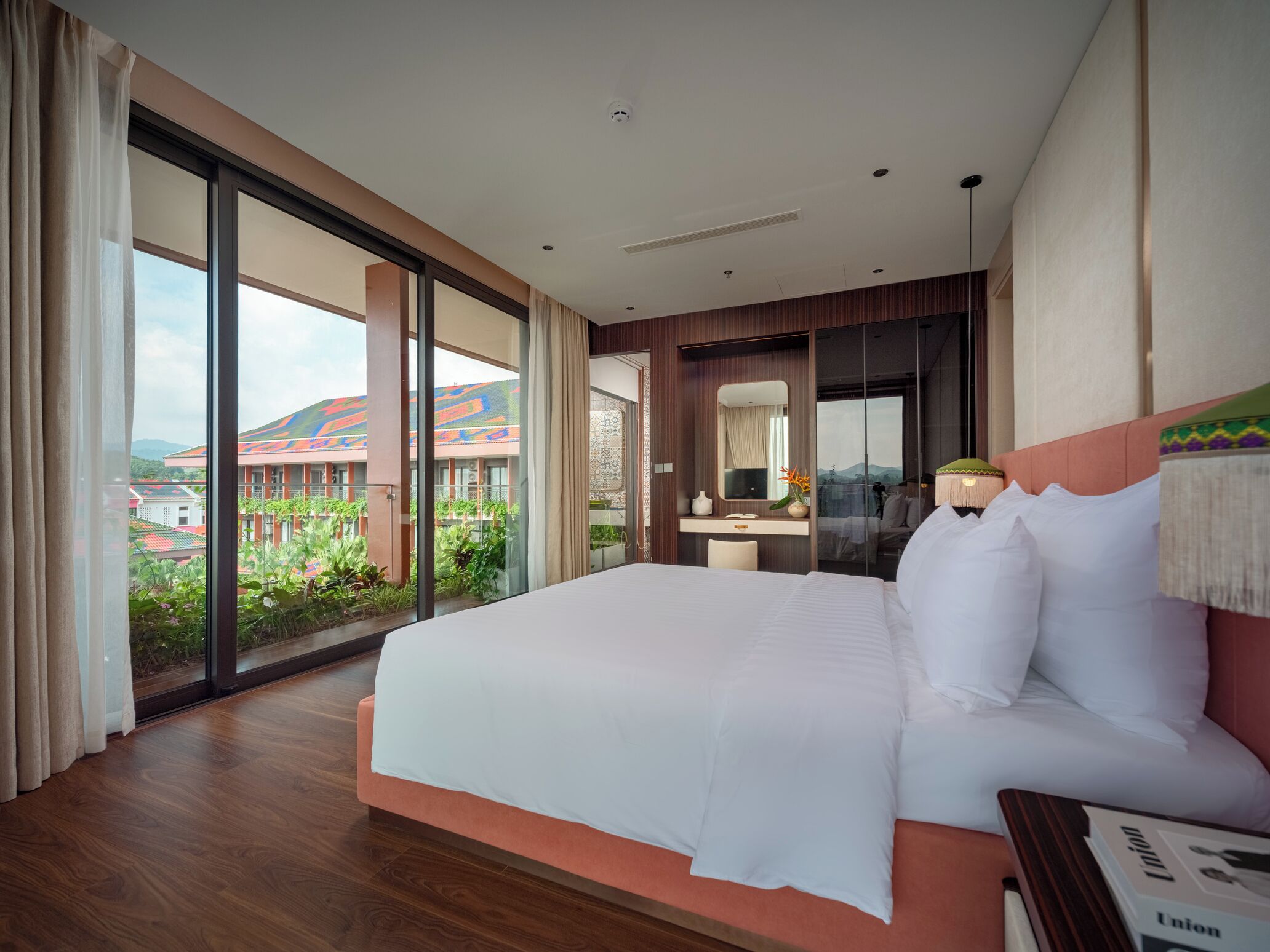 A hotel room with a large bed, a desk, and a view of a building with colorful roofs.