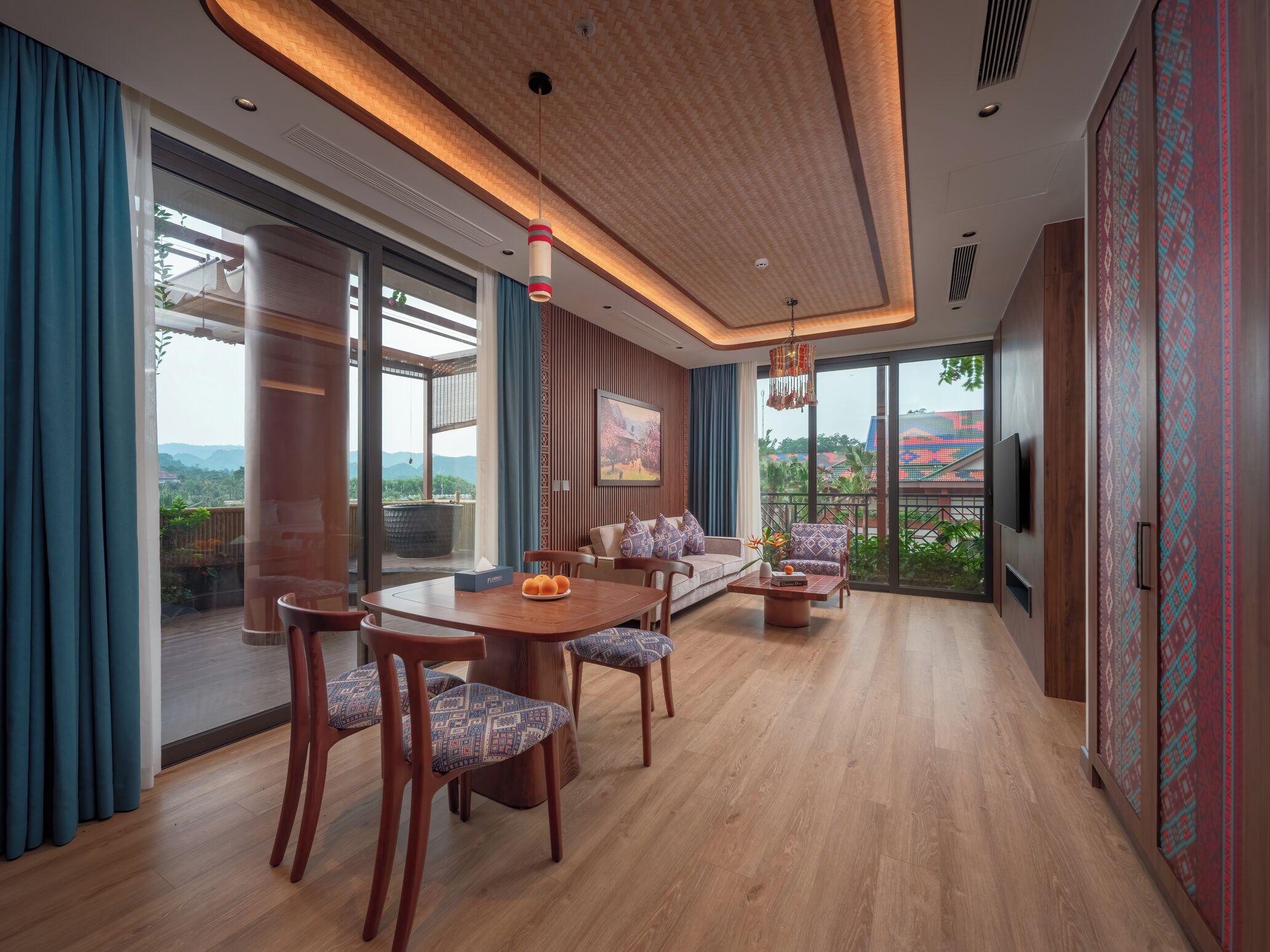 A modern living room with a wooden floor, a dining table with chairs, a sofa, and a TV mounted on the wall.
