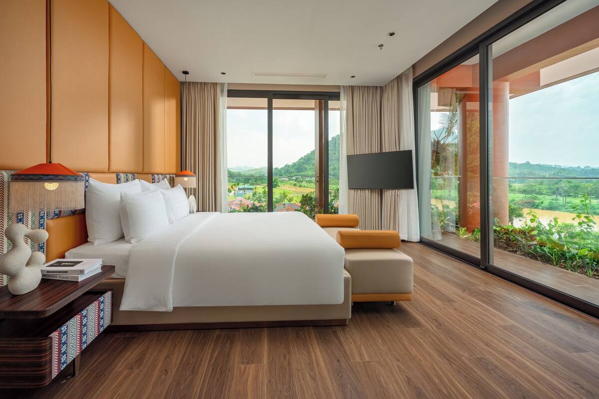 Una habitación de hotel moderna con una cama grande, un televisor y vistas a un paisaje verde.