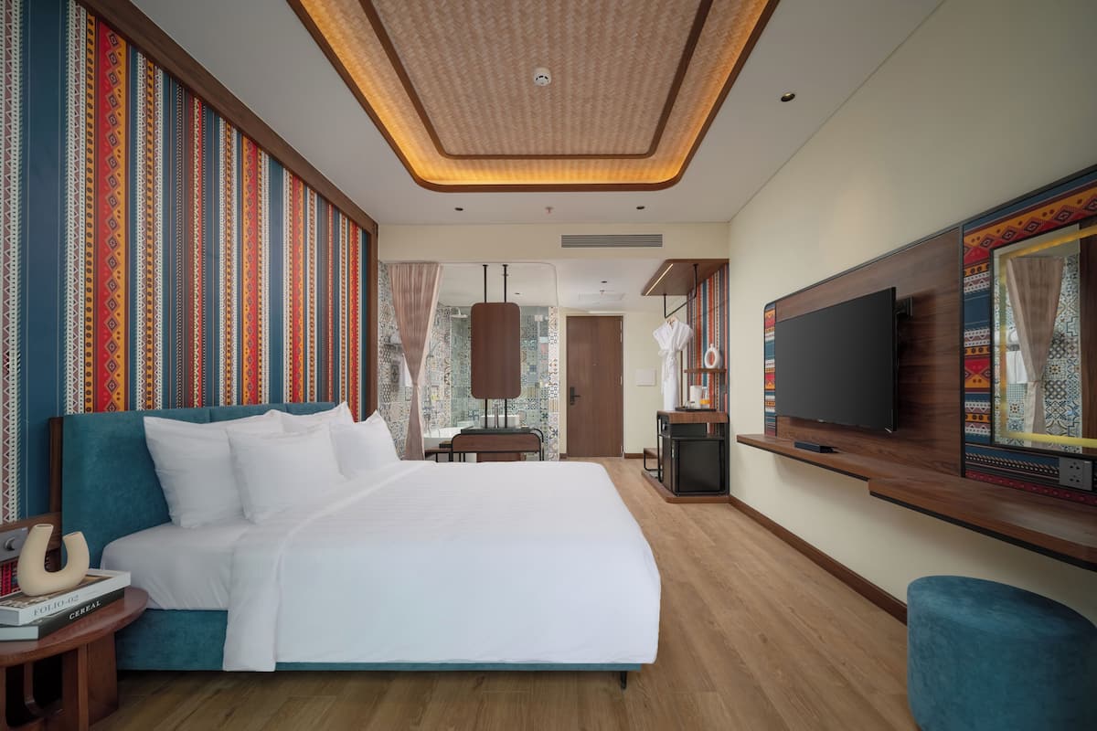 Una habitación de hotel moderna con una cama grande, un televisor montado en la pared y un escritorio pequeño.
