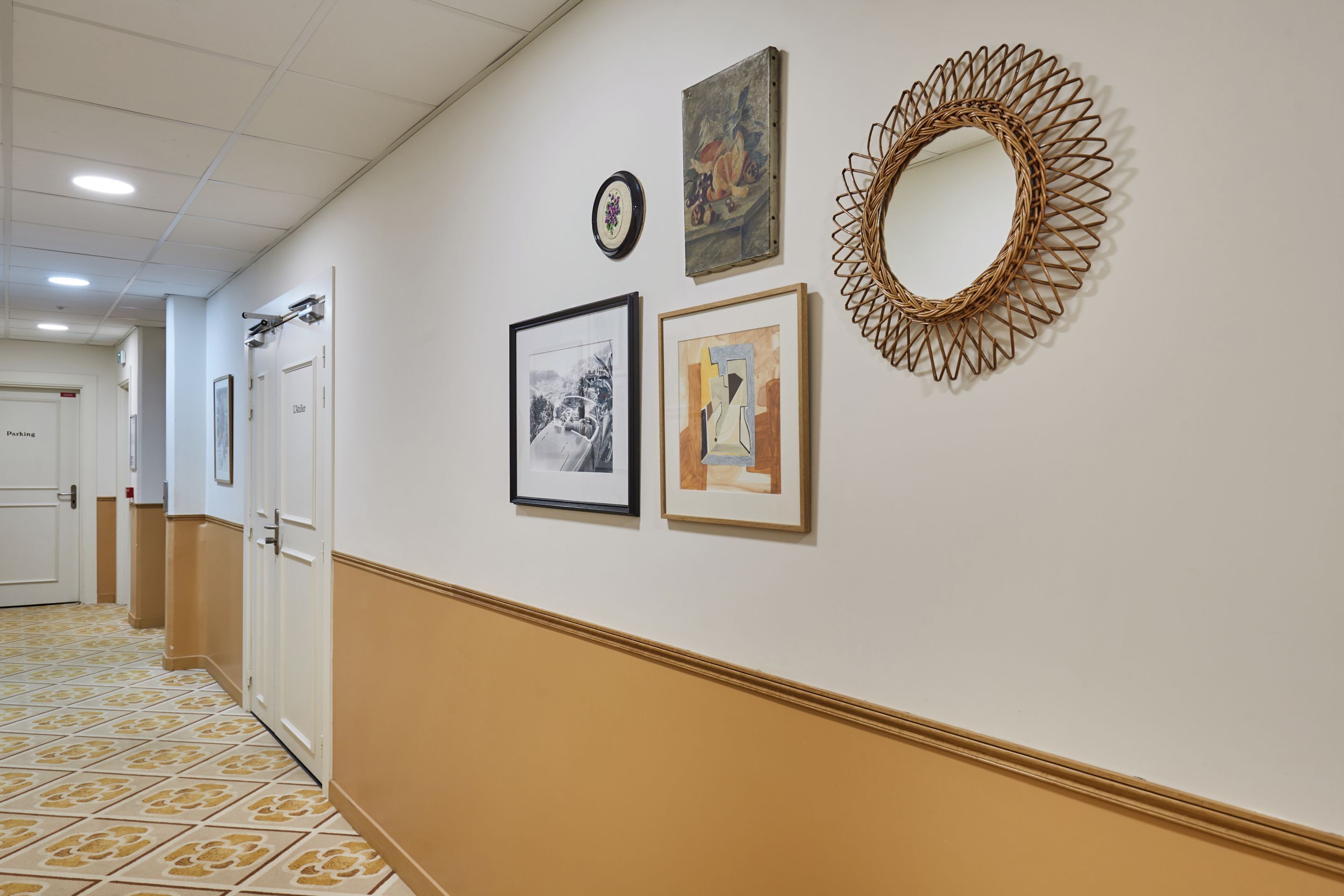 Un pasillo con obras de arte enmarcadas, un espejo y puertas que dan a habitaciones.
