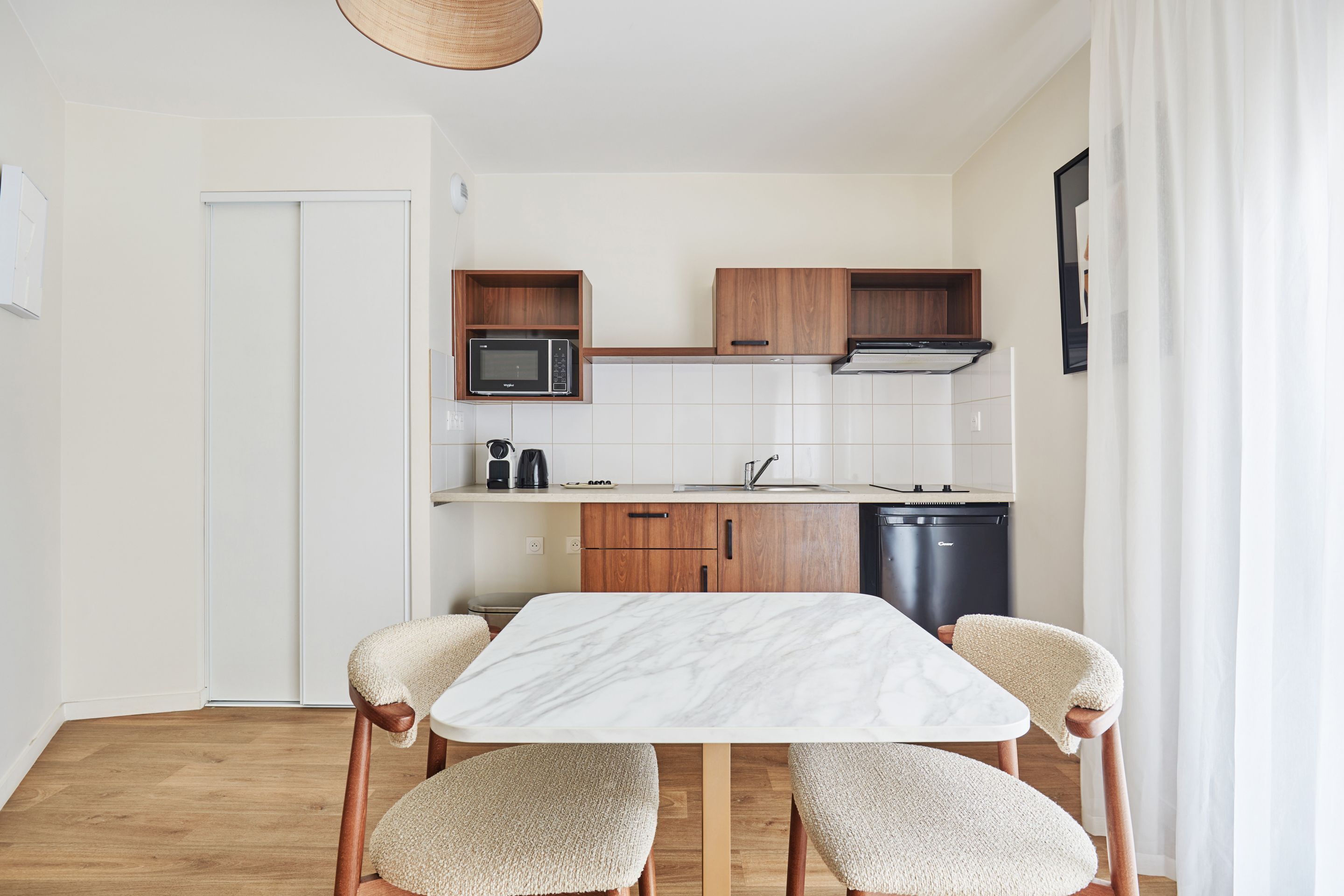 Una cocina moderna con armarios blancos, microondas y lavavajillas. Hay una mesa de comedor de madera con dos sillas.