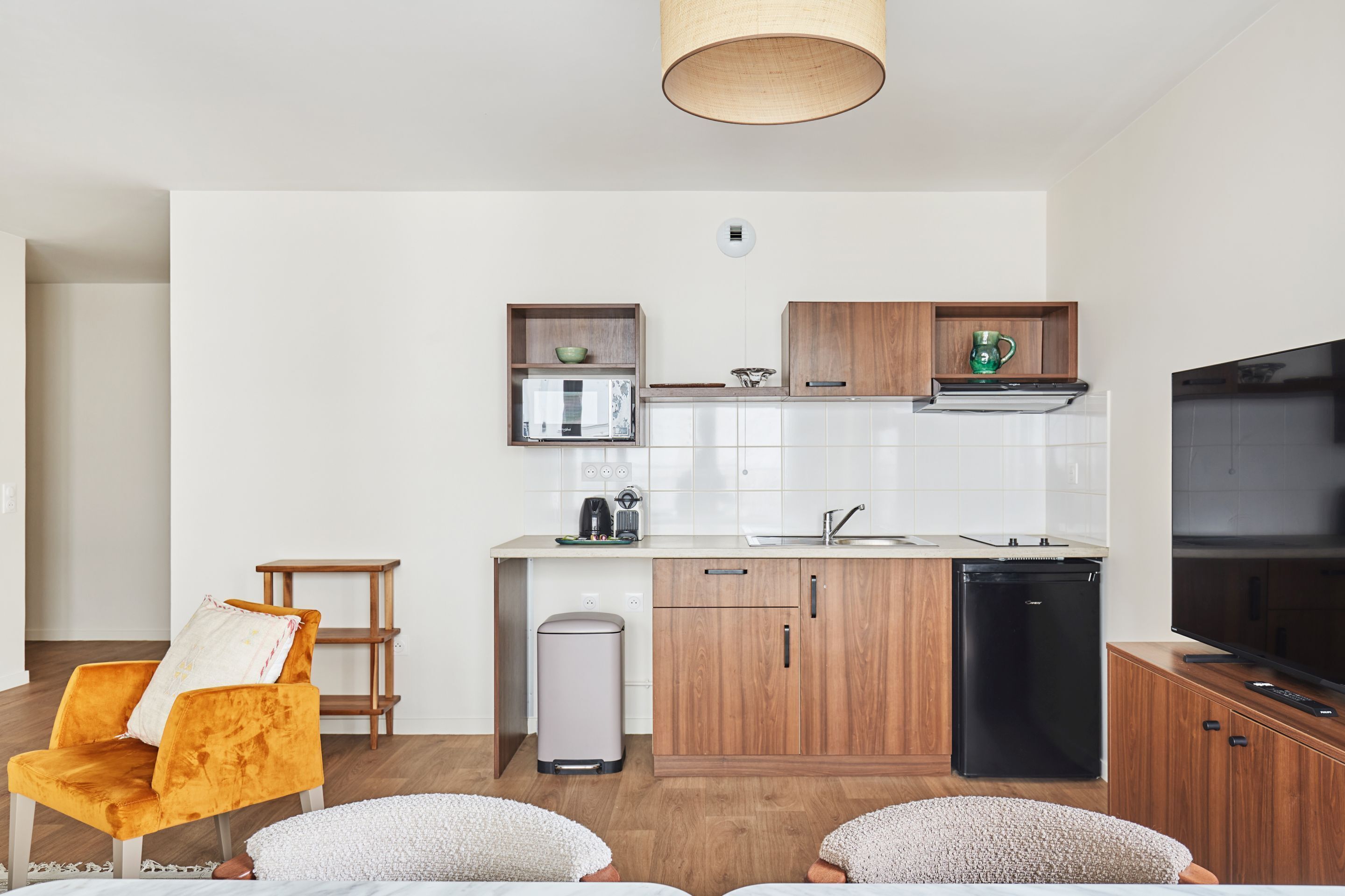 A modern kitchen with white cabinets, a black refrigerator, and a wooden countertop. There is a yellow chair and a white sofa in the living area.