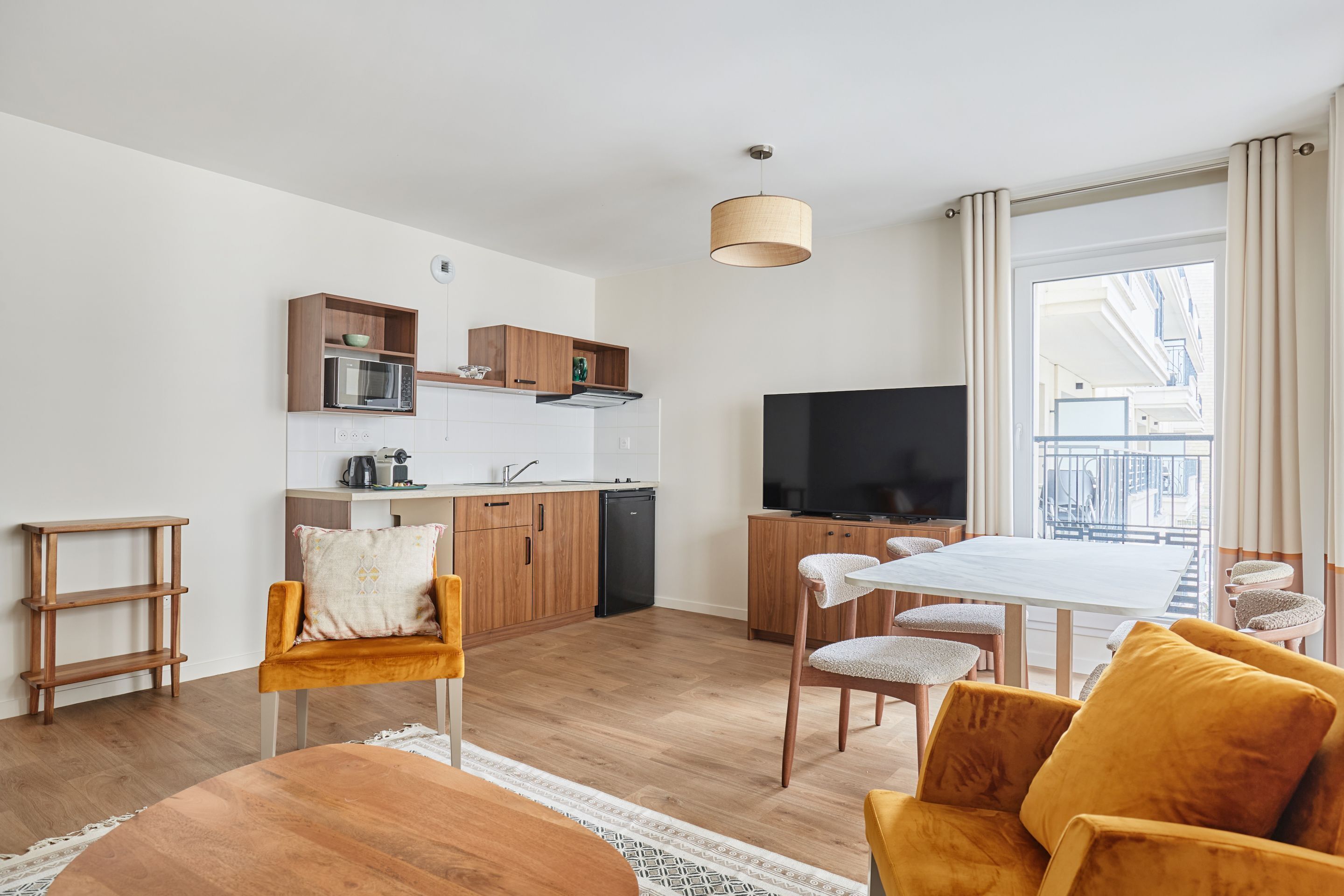 A modern apartment with a kitchen, dining area, and living room. It includes a TV, wooden furniture, and a balcony with a view.