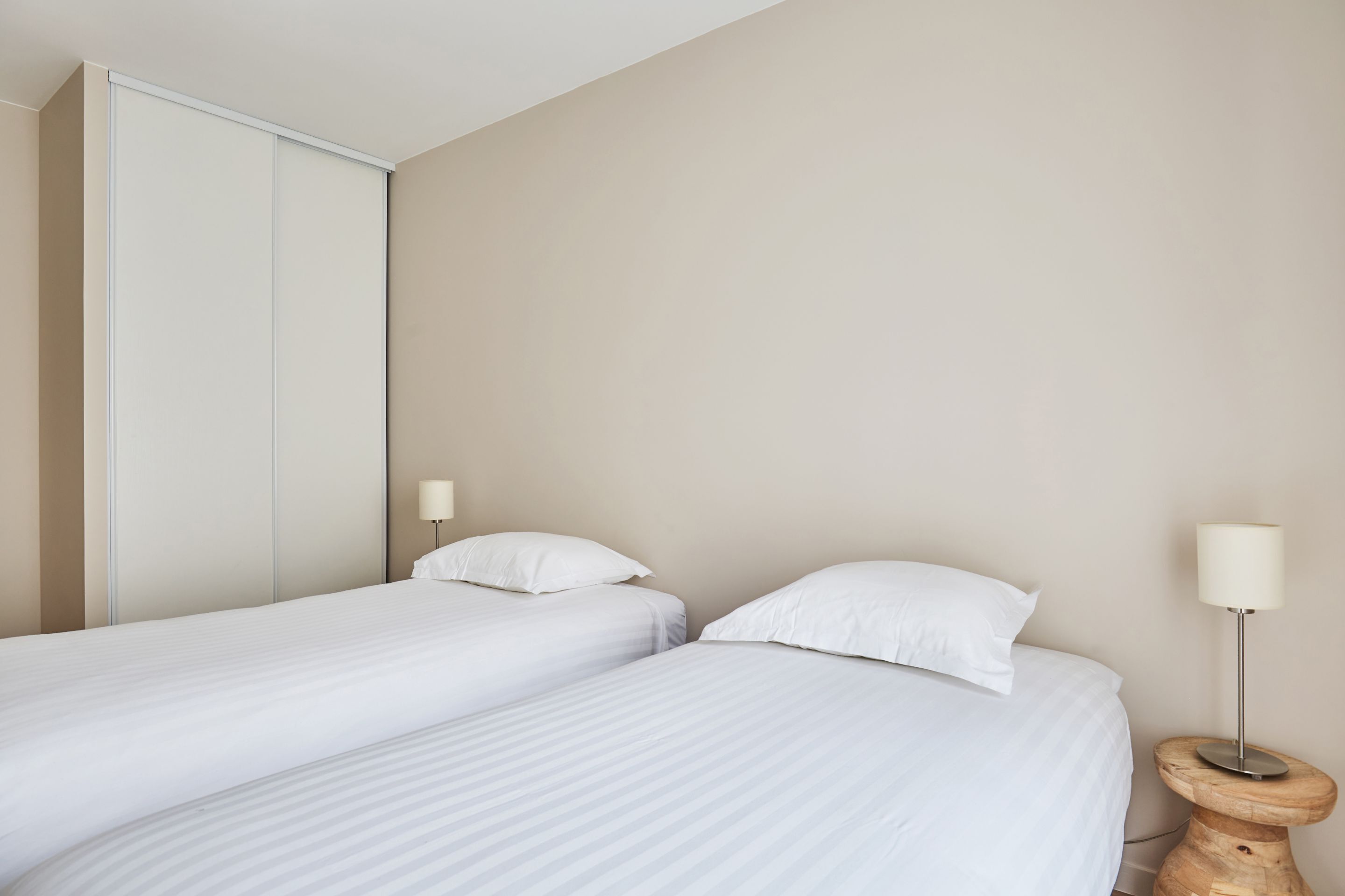 A bedroom with two single beds, a wooden nightstand with a lamp, and a sliding door closet.