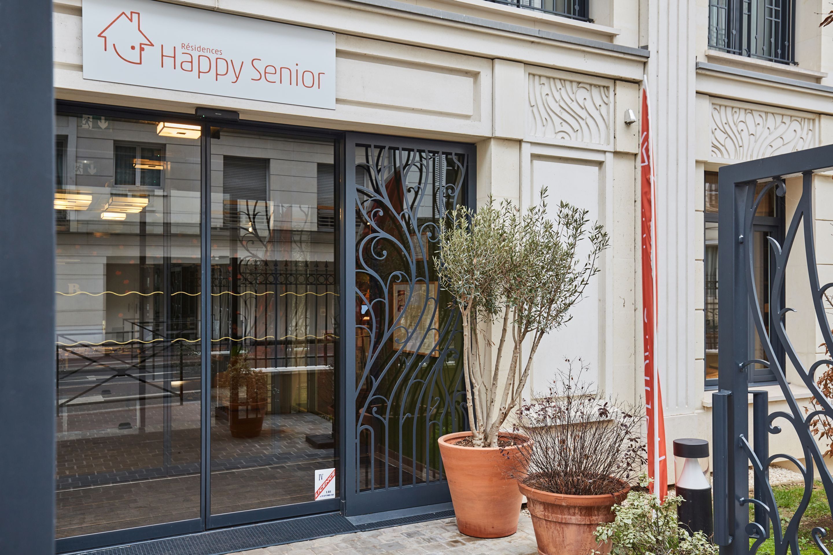 A building with a sign reading "Happy Senior" and large potted plants in front.