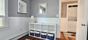 Un couloir avec une console blanche, des boîtes de rangement, un miroir et un panneau mural.
