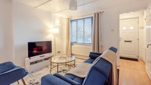 A living room with a TV, sofa, and a glass coffee table. - Cosy 2-bedroom house with Parking (Salford)