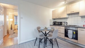 A modern kitchen with a dining table set for four, a microwave, stove, and oven. - Cosy 2-bedroom house with Parking (Salford)