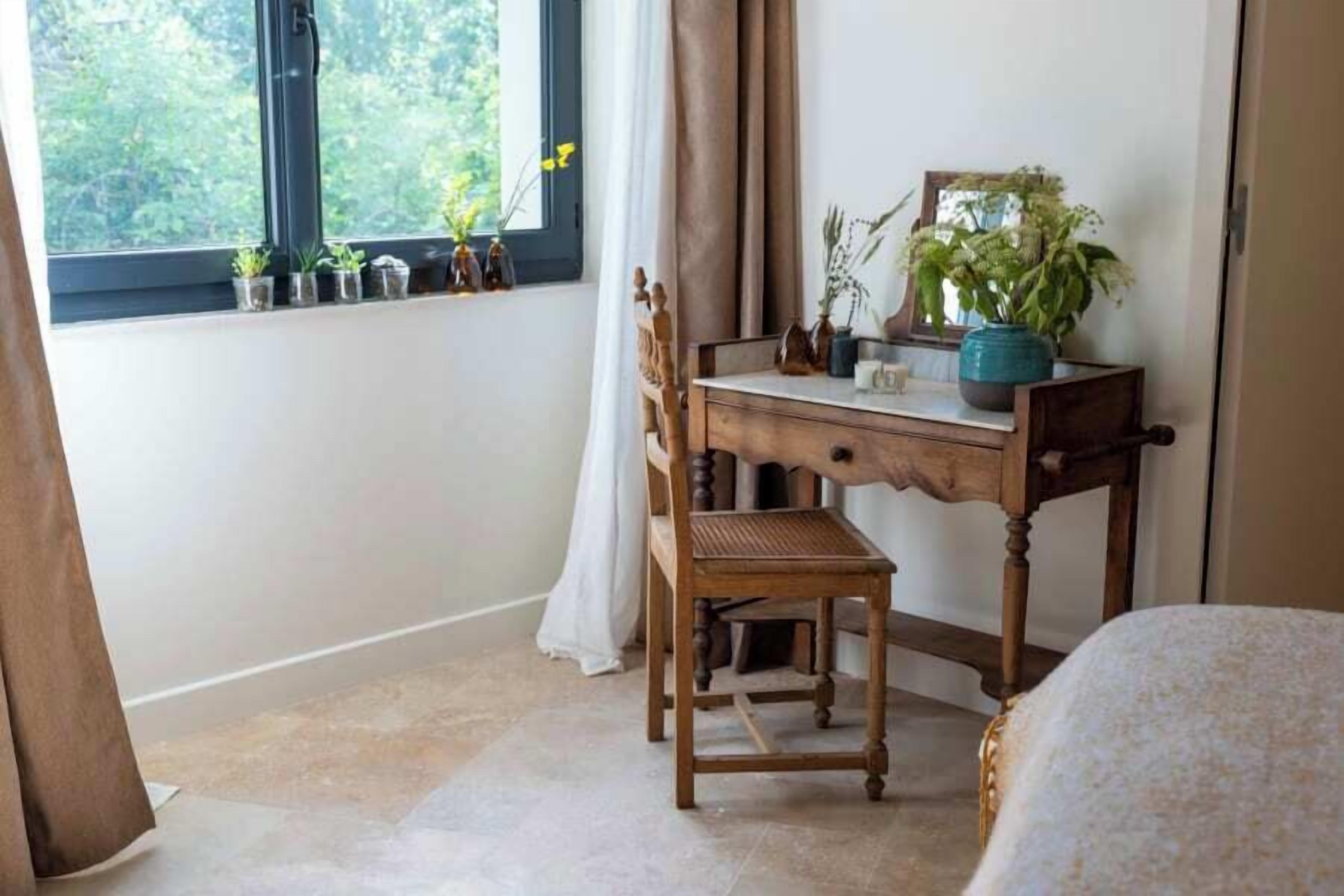 A bedroom with a wooden desk, a chair, a bed, and a window with curtains.