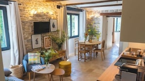 A cozy living area with a stone wall, a sofa, a coffee table, and a dining table with chairs. - Les Terres Aoyama (Saint-Julien-les-Rosiers)