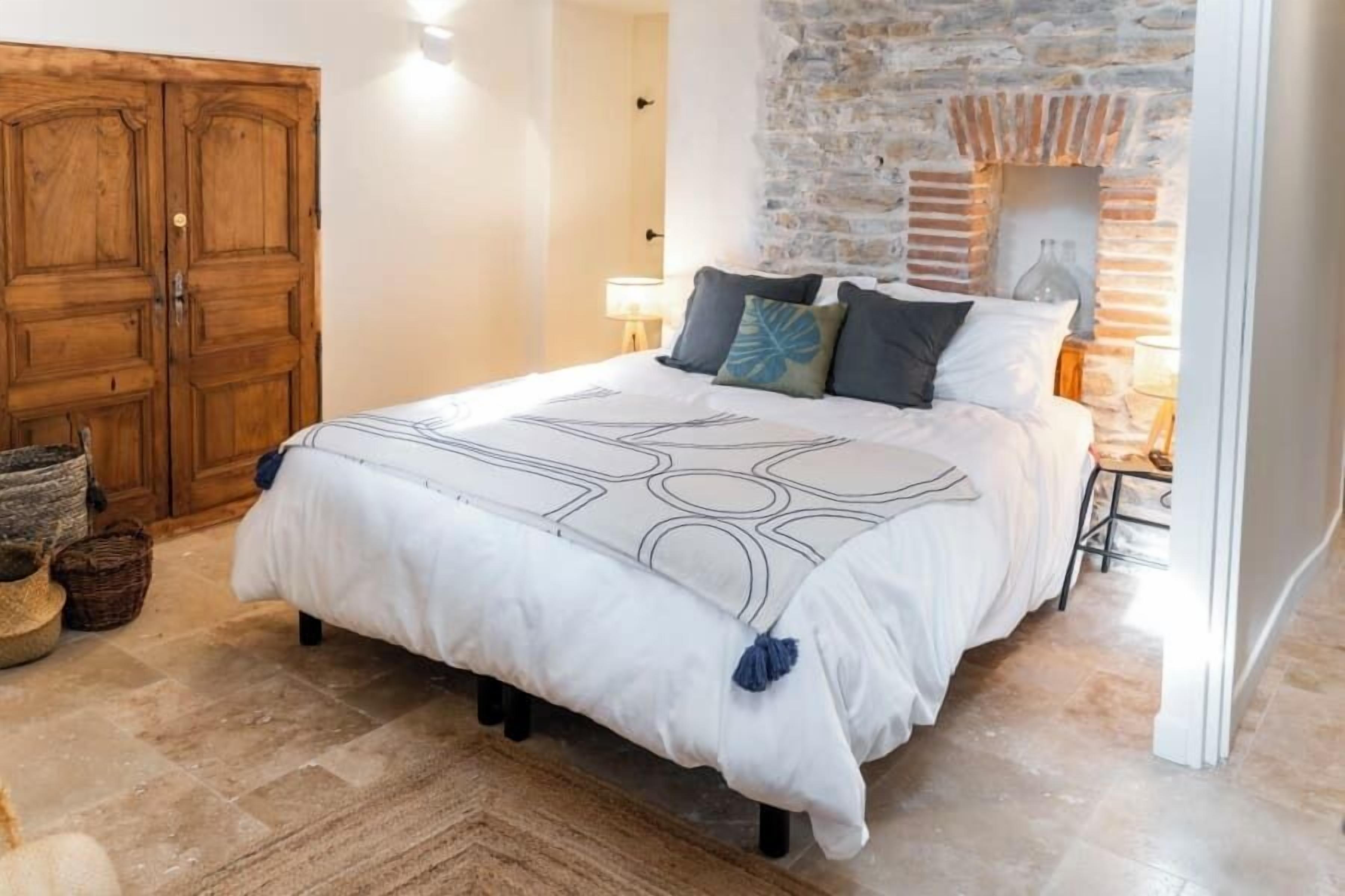 A bedroom with a large bed, a stone wall, and a wooden wardrobe.