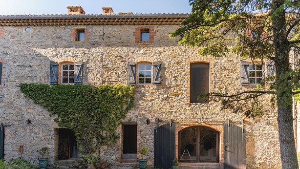 A stone building with multiple windows, a large arched doorway, and a gravel courtyard. - Les Terres Aoyama (Saint-Julien-les-Rosiers)