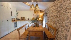 A rustic kitchen with stone walls, wooden benches, and hanging light fixtures. - Les Terres Aoyama (Saint-Julien-les-Rosiers)